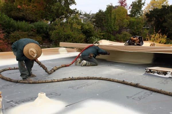 Armstrong Roofing - Two spf roofing installers spraying a flat roof