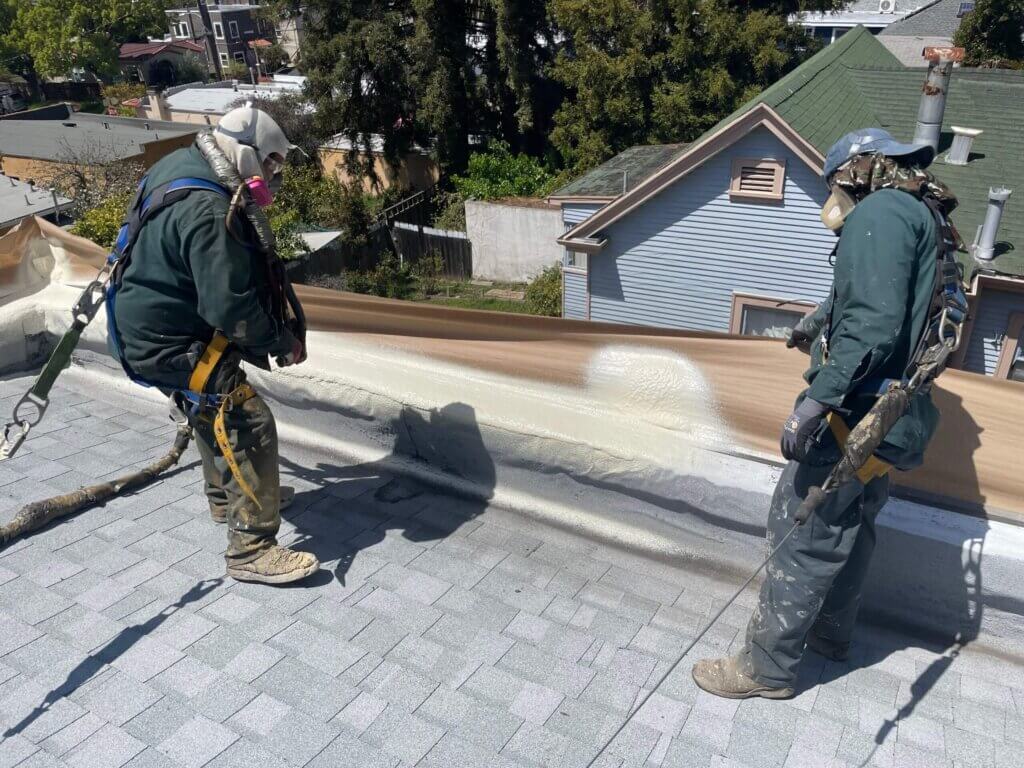 Two workers applying foam roofing material